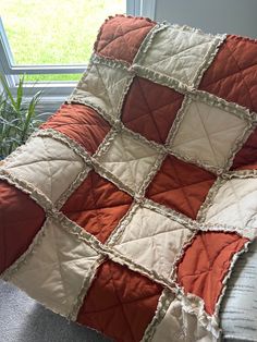 an orange and white quilt sitting on top of a couch next to a plant in front of a window