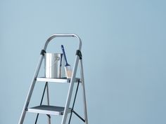 a silver step ladder with a bucket and toothbrushes on it, against a blue background