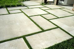 an outdoor walkway with grass in the middle and white tiles on the ground, leading to a house