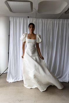 a woman standing in front of a white backdrop wearing a dress with ruffle sleeves