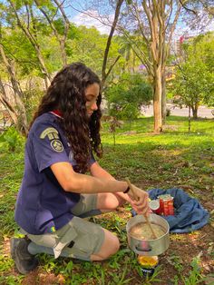 a woman sitting on the ground with food in her hand and some cans next to her