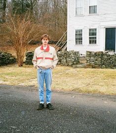 a man standing in front of a house on the side of a road with his hands in his pockets