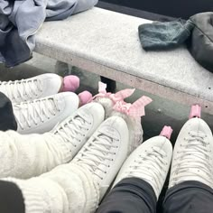 four pairs of white sneakers with pink bows on them sitting on a bench next to clothes