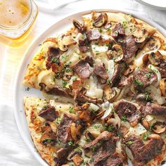 a pizza topped with meat and mushrooms on top of a white plate next to a glass of beer