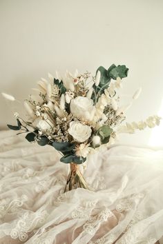 a bouquet of white flowers sitting on top of a bed next to a lace covered sheet