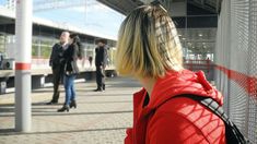 a woman in a red jacket waiting at a train station