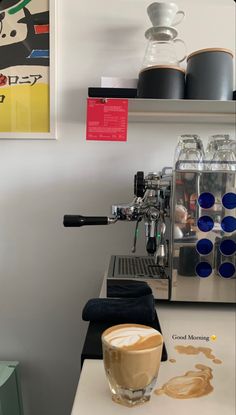 a cup of coffee sitting on top of a counter next to a machine and some cups