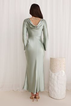 the back of a woman in a long green dress standing next to a white cake