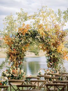 an outdoor ceremony setup with wooden chairs and flowers on the arch, overlooking a body of water