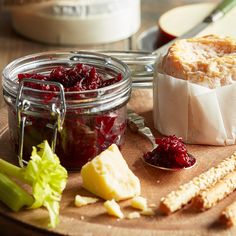 cheese, cranberry sauce and crackers on a cutting board next to bread