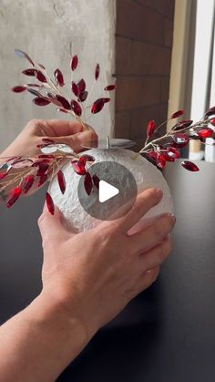 a person holding a vase with red flowers on it and another hand reaching out to the vase