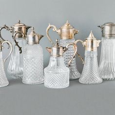 an assortment of glass and silver items on a gray surface with one gold - plated coffee pot