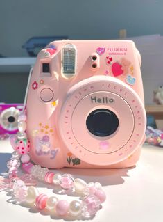 a pink camera sitting on top of a table next to some beads and other items