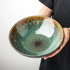 a person holding a green and brown bowl with white paper in it's center