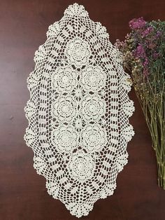 a crocheted doily next to dried flowers on a wooden table with brown background