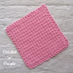 a pink crochet square sitting on top of a white table next to a brick wall