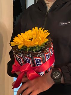 a man in black jacket holding a chocolate cake with sunflowers and candy bars