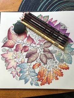 some colored pencils are laying on top of a drawing book with leaves and flowers