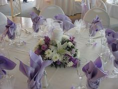 the table is set with purple and white flowers, candles, and napkins on it