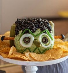 a plate topped with chips and a green monster face on top of it, surrounded by tortilla chips