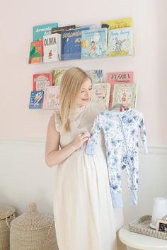 a pregnant woman holding up a baby's shirt in front of bookshelves