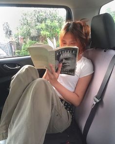 a woman sitting in the back seat of a car reading a book while holding an open book