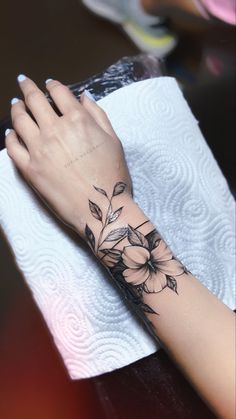 a woman's hand with a flower tattoo on her left arm and the wrist