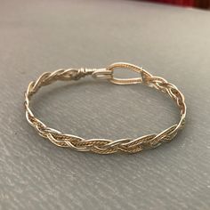 These bracelets are braided using a standard three-strand pattern, just like you would use when braiding hair or rope. The large hook and eye closure is part of the entire design, and allow the wearer to hook and unhook the bracelet with one hand; no helper should be needed! I have two variants: silver with a twisted gold wire as an accent and gold with a twisted silver wire. I make them in a range of sizes (in 1/4 inch increments) to fit any wrist. Yes! Sizes!! To determine the size you need, m