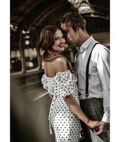 a man and woman standing next to each other in front of a train station with their arms around each other