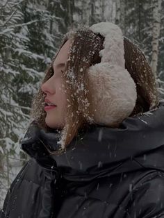 a woman standing in the snow wearing a black coat and a white hat on her head