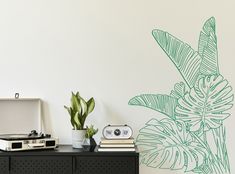 a green plant sitting on top of a black dresser next to a wall with a stencil