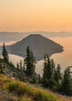 the sun is setting over an island in the middle of a lake surrounded by pine trees