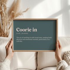 someone holding up a sign that says coorie in front of a white couch