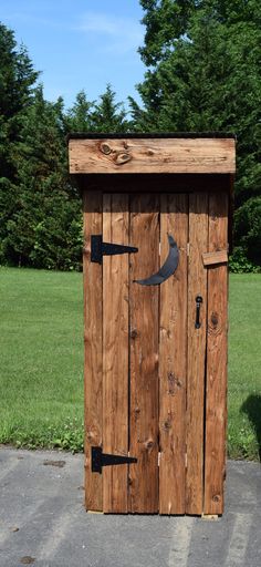 a wooden outhouse sitting on the side of a road in front of some trees