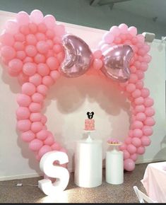 a balloon arch with pink balloons and minnie mouse ears on the top, along with an s shaped cake