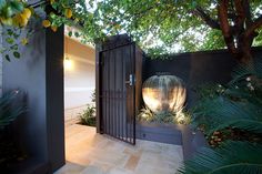 a gated entrance to a house with plants and trees in the foreground, next to a large potted planter