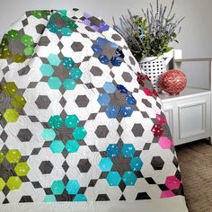 a bed with a colorful quilt on top of it next to a potted plant