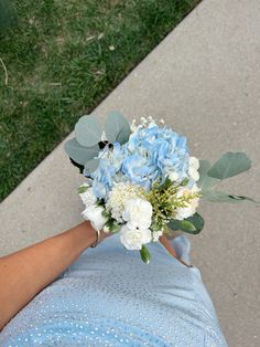 a person holding a blue and white bouquet in their hand on the sidewalk with grass behind them