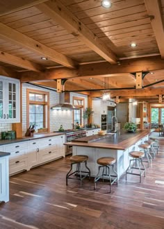 a large kitchen with wooden floors and white cabinets, an island countertop and bar stools