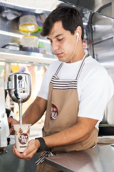 a man in an apron is pouring something into a cup with a blender behind him