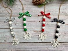 three christmas ornaments hanging from strings on a wooden table with pine cones and snowflakes