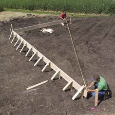 two men work on building a wooden structure in the middle of a dirt field,