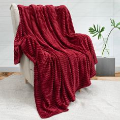 a red blanket sitting on top of a white chair next to a potted plant