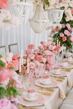 the table is set with pink flowers and white china dishes, candles, and teacups