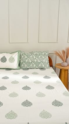 a bed with green and white sheets on it next to a wooden chair in front of a wall