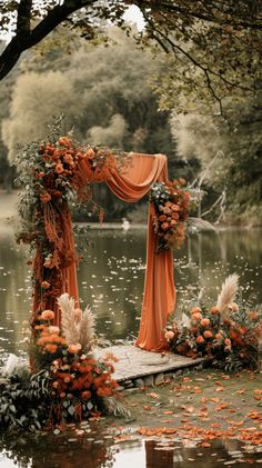 an outdoor wedding setup with orange draping and flowers on the water's edge