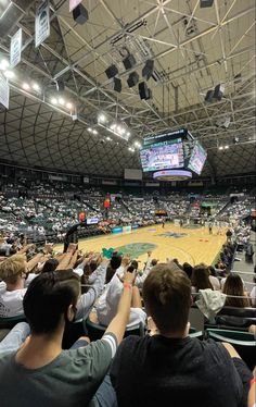 an indoor basketball court with people sitting on the seats and one person holding up his cell phone