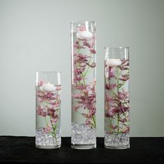 three tall vases filled with water and flowers