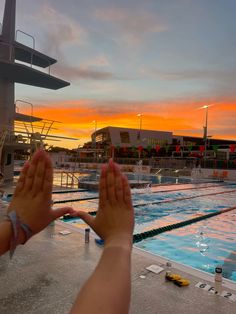 two people are holding their hands up in front of an empty swimming pool at sunset