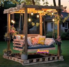 an outdoor swing bed made out of pallets with lights hanging from the ceiling and pillows on it